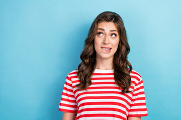 Fototapeta premium Closeup photo of young funny nervous excited pretty lady wear red stiped t-shirt curly hair bite lips looking empty space oops isolated on blue color background