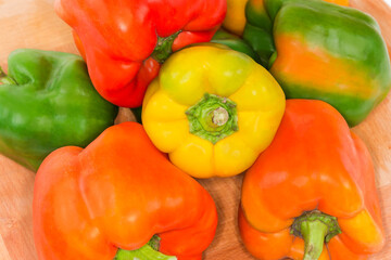 Multicolored bell peppers on the wooden surface, fragment top view