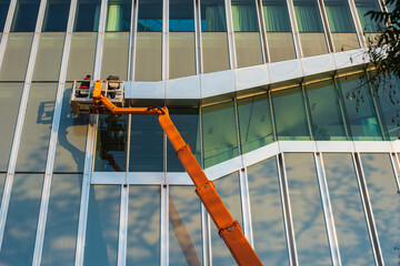 Cleaner worker using a cherry picker to clean a glas facade of a contemporary office building.