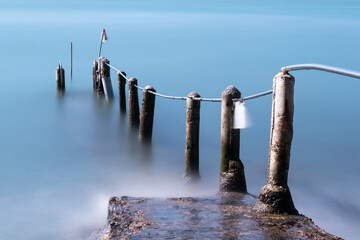 Old broken pier leads into the sea from the beach at Sandy Bay, Hong Kong Island.  The posts and rails are bent and twisted. Long exposure gives smooth sea surface.