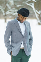 Sad african man stay in winter in snowy park. Young man in beret posing for camera outdoor.