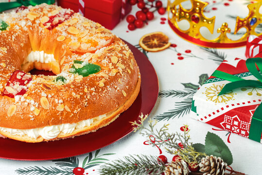 Roscon de reyes with cream and christmas ornaments on a red plate. Kings day concept spanish three kings cake.Typical spanish dessert for Christmas