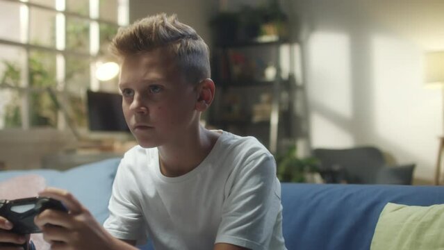 Chest up shot of teenage boy sitting on sofa at home and playing video game with excitement