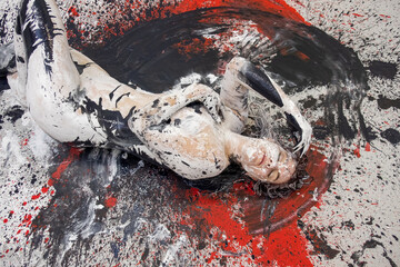 Young artistically abstract painted naked woman with black and white paint, lying on the red, black, gray designed floor in the studio