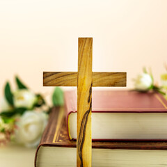 Religion card with wooden cross with closed red Christian bibles with white flowers on a light gradient background. Easter holiday. Christian religion concept. Front view