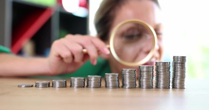 Emotions of excited greedy business woman looking at growing stack of coins through magnifying glass