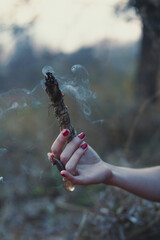 Close up smudging stick and smoke concept photo. Cleansing magical ritual. Side view photography with female hands on background. High quality picture for wallpaper, travel blog, magazine, article