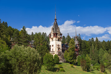 Fototapeta na wymiar Located on the southern sunny slope of hill, surrounded by centuries-old coniferous and deciduous trees, open to sky and sun, Peles Castle is pearl in this bosom of nature, Sinaia, Romania 