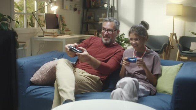 Excited middle aged father and teenage daughter having fun while playing video game together at home