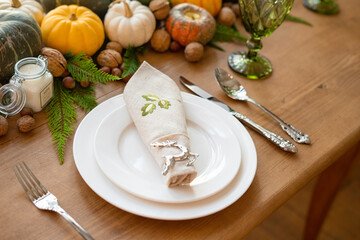 Thanksgiving table set. Plate, wine glass, cutlery and a self-paper on a wooden table. Table decoration of pumpkins, nuts, candles and juniper with copy space.