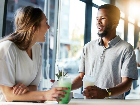 Restaurant, date and couple drinking milkshake while talking, bonding and laughing together. Happy, love and interracial man and woman in conversation while enjoying smoothie at a cafe in the city. - Powered by Adobe