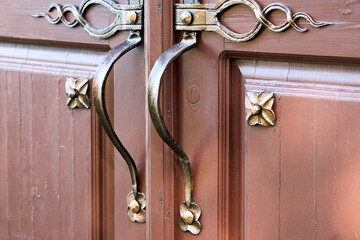 Brown wooden entrance door with gold-plated forged handles and ornate outside.