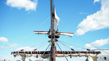 Bottom view of a ship mast with white sails against a blue sky