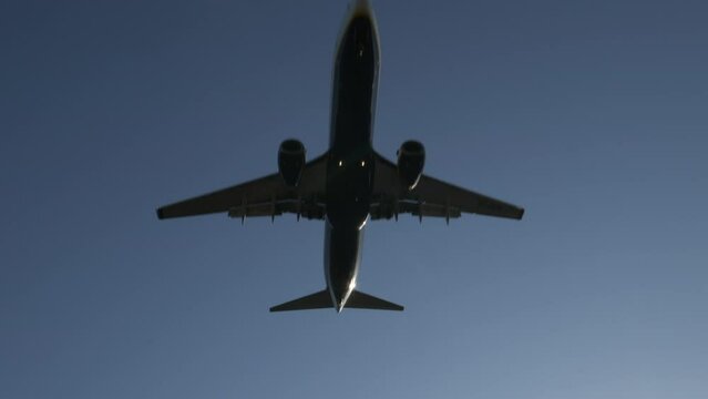 Big commercial airplane passing above camera against blue sky, low angle, tilt