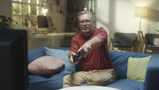 Medium shot of joyous middle aged man playing exciting video game while spending time at home