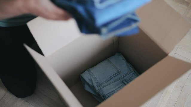 Person is putting neatly folded jeans into carton boxes to donate to charity.