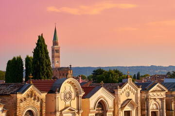 Blick über einen Friedhof in Pieve di Soligo im letzen Abendlicht . Im Hintergrund der Kirchturm von Parrocchia del Duomo Santa Maria Assunta
