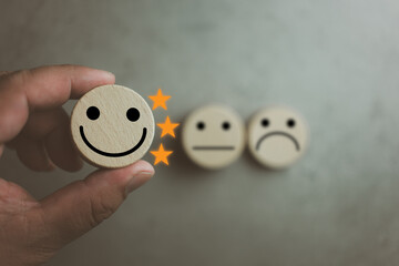 Customer satisfaction survey concept. Customer selects wooden cube with happy face icon and three...