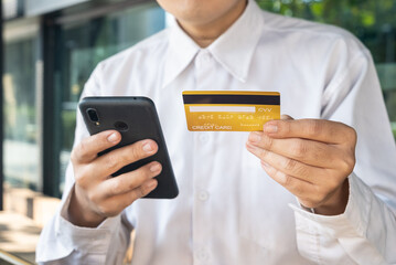Close-up hand of asian man using cellphone and gold credit card for online payment, online shopping, mobile banking, money transfering. cropped image.