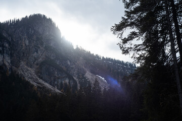 The sunlight is shining between the peak of a rocky mountain at Lake Tovel, Northern Italy