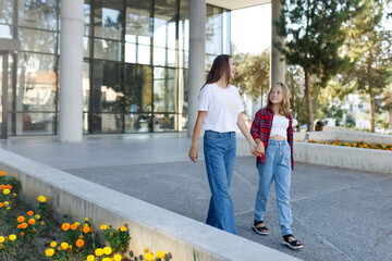 Woman walking and chatting with daughter schoolgirl after school outdoors. Cheerful teen female speaking with mother in good mood. Talk concept
