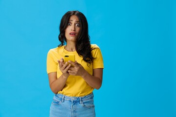 Woman with a phone in her hands with a yellow case on a blue background in a yellow T-shirt,...
