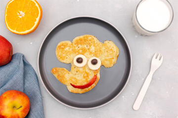 Funny elephant face shape snack from pancake on plate. Cute kids childrens baby's sweet dessert, healthy breakfast,lunch, food art with milk,apples,orange on gray concrete background,top view
