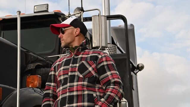 Caucasian Commercial Semi Truck Driver in His 40s in Front of a Vehicle. Ground Transportation Theme.