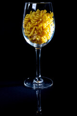 raw pasta in glass jar, wine glass. in bucket. raw pasta on black background. front view raw pasta, dropped from hand, place for text, yellow long spaghetti straws,