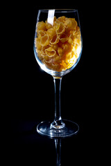 raw pasta in glass jar, wine glass. in bucket. raw pasta on black background. front view raw pasta, dropped from hand, place for text, yellow long spaghetti straws,