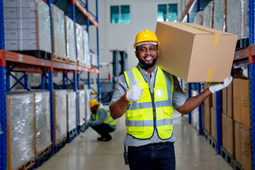 African American warehouse worker carry the box on his shoulder and show thumbs up to camera with...