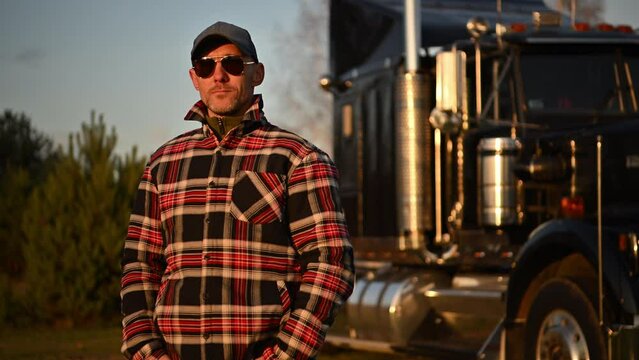 Truck Driver Wearing Sunglasses and Baseball Hat Staying in Front of His Semi Truck