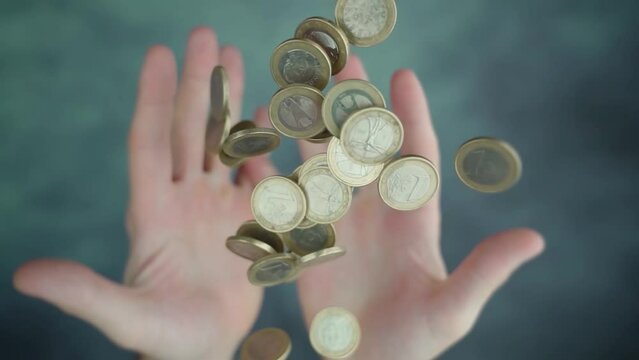 Both hands of person throwing up pile of steel Euro coins over blurred green-colored table in bright studio macro slow motion
