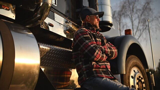 American Caucasian Trucker Seating on His Semi Truck Steps. Ground Transportation Industry Worker.