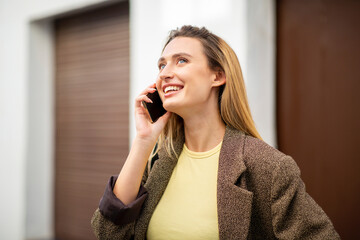 Happy young woman looking up while talking on smart phone in city