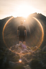 A person is framed inside the lens flare of the camera during sunset on top of a mountain