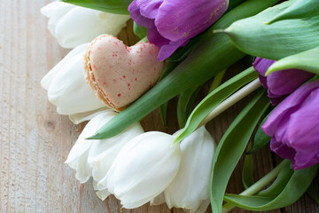 One creamy cookie on the white and purple tulips. A bouquet of tulips with one macaroon is on the wooden background. Romantic