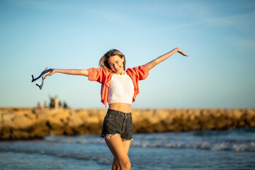 Cheerful young woman with arms raised by beach