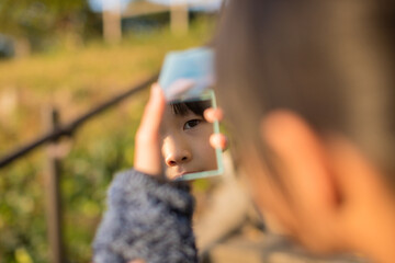 秋の公園で遊んでいる子供が手鏡を見ている様子 - obrazy, fototapety, plakaty