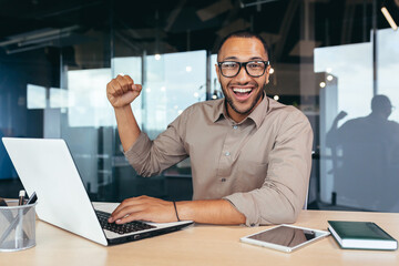 Portrait of successful hispanic executive, man in glasses smiling and looking at camera holding hand up gesture of achievement, good work result, victory and triumph.