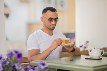a cute man is drinking tea in a cafe on the street, a sexy guy is having breakfast in a cafe