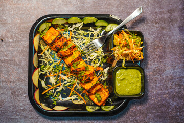 Paneer tikka is an Indian dish made from chunks of paneer with sauce and  vegetables on the table