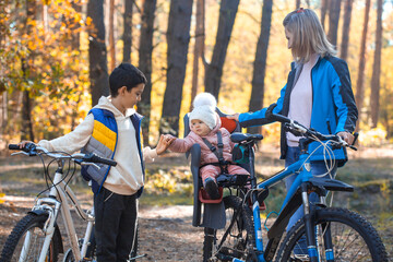 Plakat children with mom ride a bike oneautumn day in a pine forest