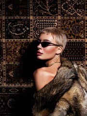 Portrait of a naked woman in sunglasses in a fur coat on the background of a carpet