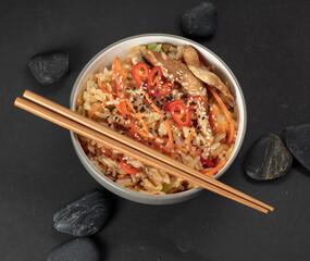 Traditional asian frying noodles with prawns and mussels in a black bowl and chopsticks on a black slate background with decorate stones, top view 
