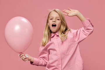 Obraz na płótnie Canvas a happy, joyful school-age girl stands on a pink background with a big balloon raising her hand up. Horizontal photo with blank space for advertising layout insert