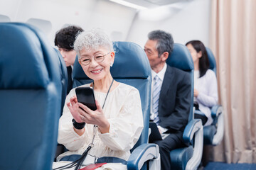 飛行機でスマホを使うシニア女性