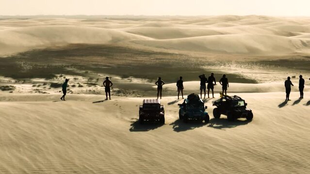 People in silhouette on high sand dune, windy conditions on buggy tour; aerial