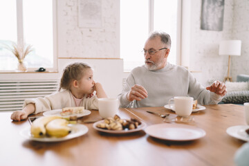 Senior man and little girl having breakfast and talking