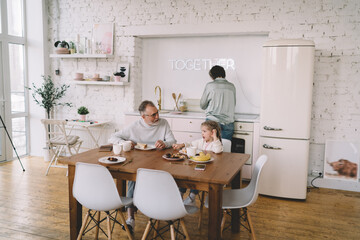 Happy grandfather having breakfast with granddaughter in kitchen